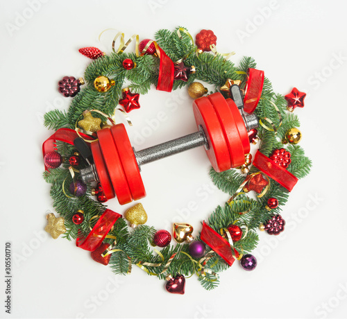 Christmas or New Year on a white background. Composition with dumbbells, gift, red and gold glass balls, fir tree branches for healthy lifestyle and sport