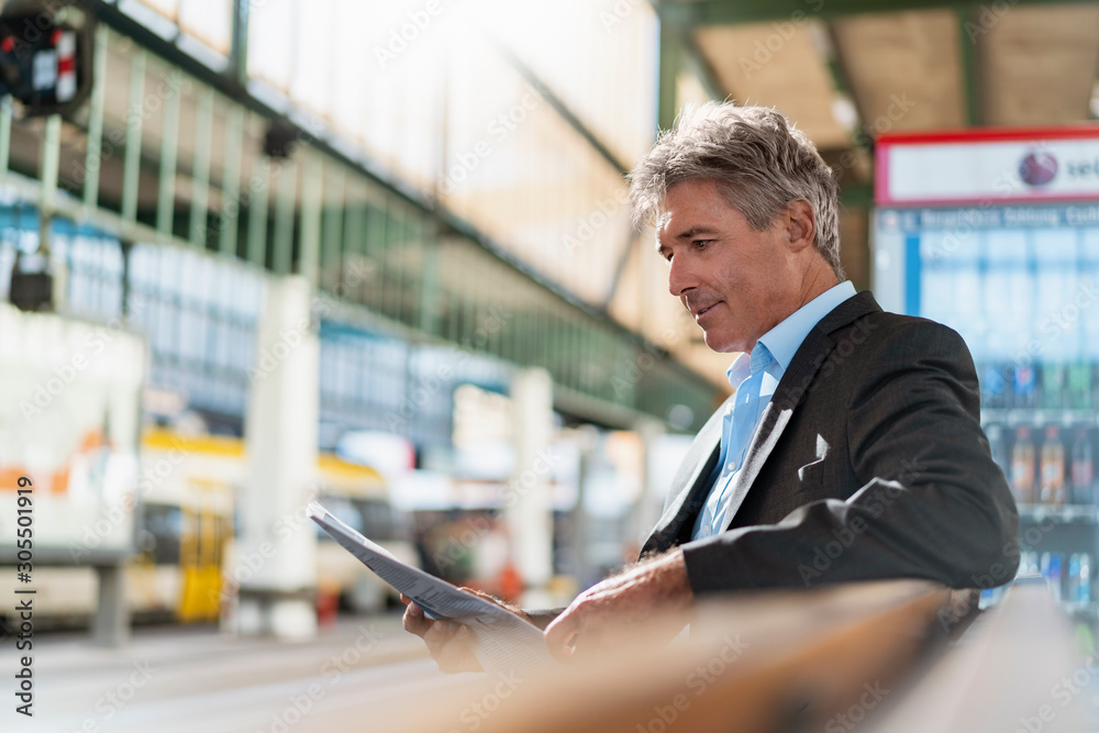 Mature businessman reading newspaper on station platform Mature businessman reading newspaper on station platform
