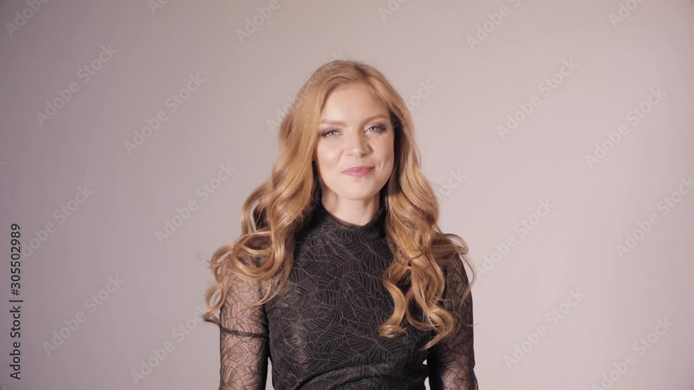 Young beautiful woman looking at camera, demonstrating her hair and enjoying it. Blonde pretty lady in black dress touching gorgeous bright curls. Happy smiling girl turning round and shaking head. Young beautiful woman looking at camera, demonstrating her hair and enjoying it. Blonde pretty lady in black dress touching gorgeous bright curls. Happy smiling girl turning round and shaking head.