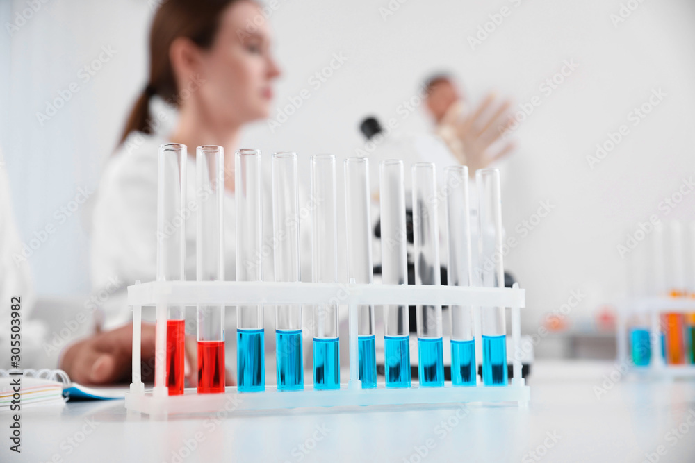 Rack with test tubes on white table and laboratory assistants in room. Medical research Rack with test tubes on white table and laboratory assistants in room. Medical research