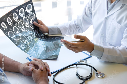 Doctor holding and looking at x-ray film examining at brain by ct scan of patient and analyze result while discussing explaining problem of medical
