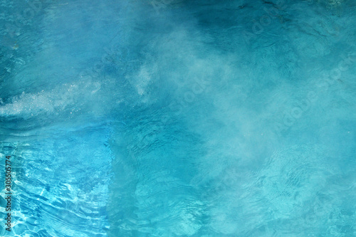 Pure clear water in the thermal pool. Hot water flows and fog rises above the pool, steam. Blue water, beautiful background.