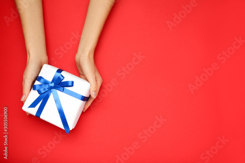 Gift box with ribbon in female hands on red background