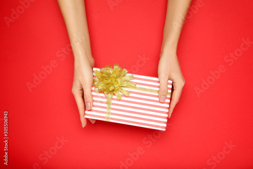 Gift box with ribbon in female hands on red background © 5second