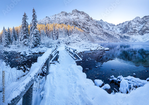 Wooden bridge covered with snow on mountain lake