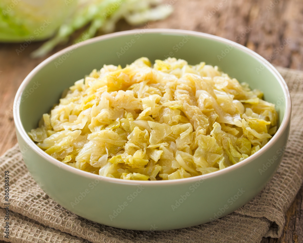 Fresh homemade braised white cabbage in bowl, raw cabbage in the back (Selective Focus, Focus one third into the cabbage) Fresh homemade braised white cabbage in bowl, raw cabbage in the back (Selective Focus, Focus one third into the cabbage)