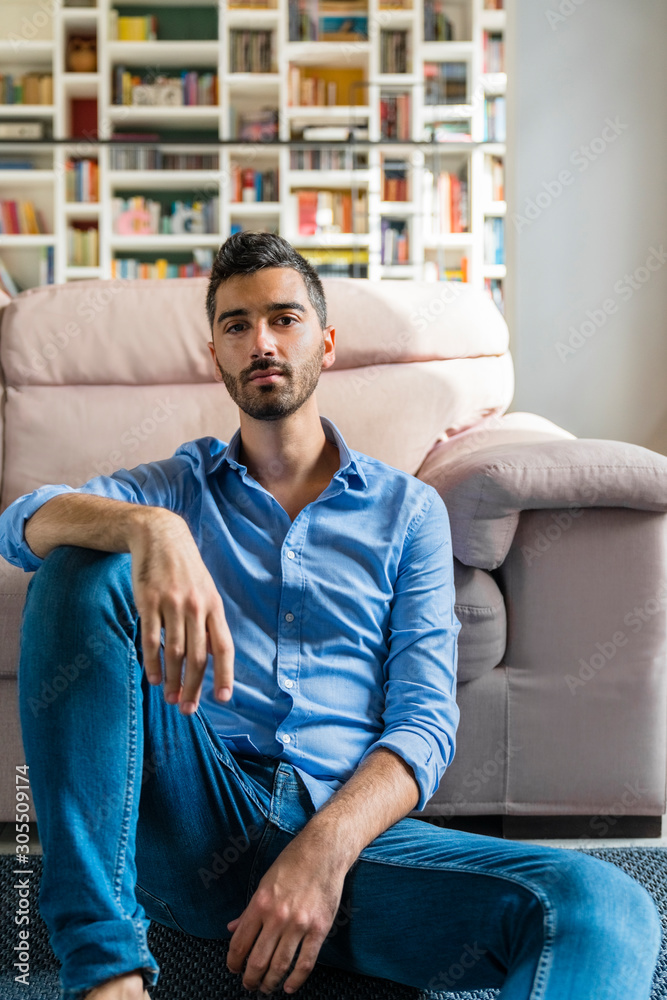 Portrait of serious young man sitting on the floor of living room at home Portrait of serious young man sitting on the floor of living room at home