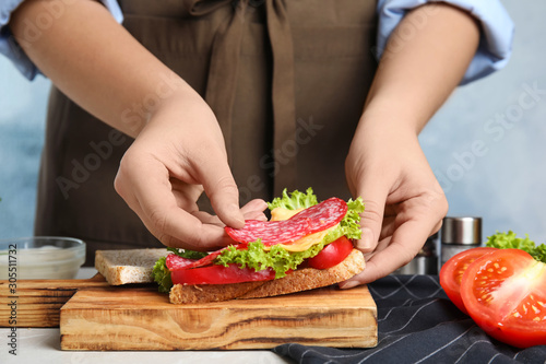 Woman making tasty sandwich with sausage at table, closeup