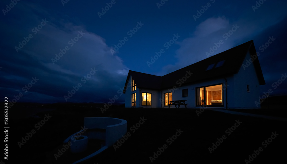 The warm glow of lit rooms from a remote Scottish Highland croft, bungalow at dusk in winter. - obrazy, fototapety, plakaty 