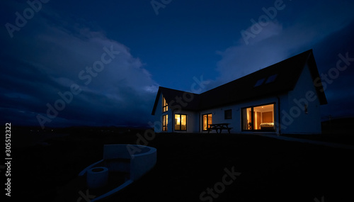 Valokuva The warm glow of lit rooms from a remote Scottish Highland croft, bungalow at dusk in winter