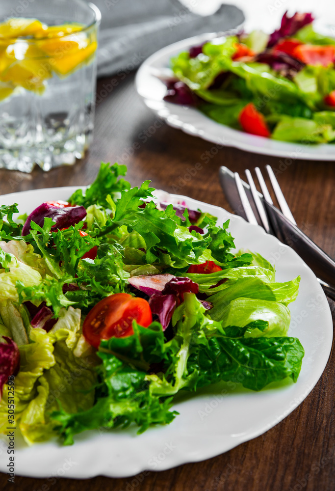 various fresh mix salad leaves with tomato in white plate on wooden background. various fresh mix salad leaves with tomato in white plate on wooden background.