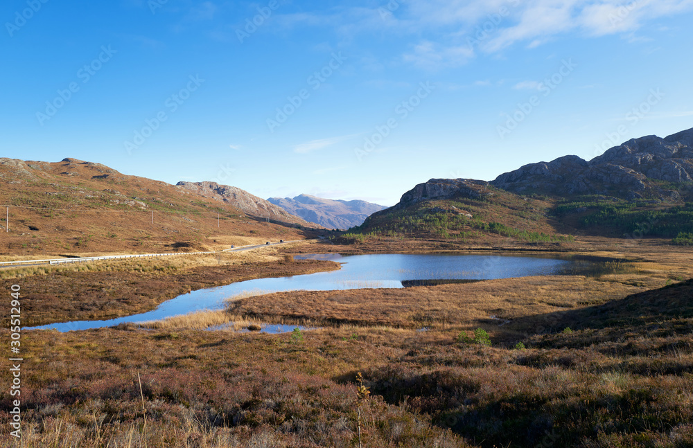 Views of Am Feur Loch in the centre and the A832 road on the left with Meall Lochan a Chleirich on the right on a sunny blue sky winters day in the Scottish Highlands.