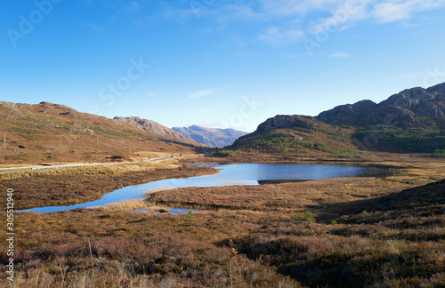 Views of Am Feur Loch in the centre and the A832 road on the left with Meall Lochan a Chleirich on the right on a sunny blue sky winters day in the Scottish Highlands.