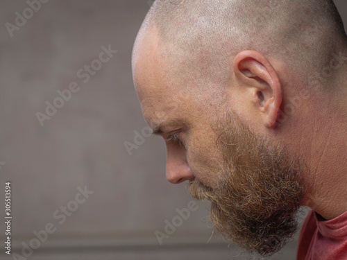 Portrait of a bald man with a beard bowing his head and looking down. side view