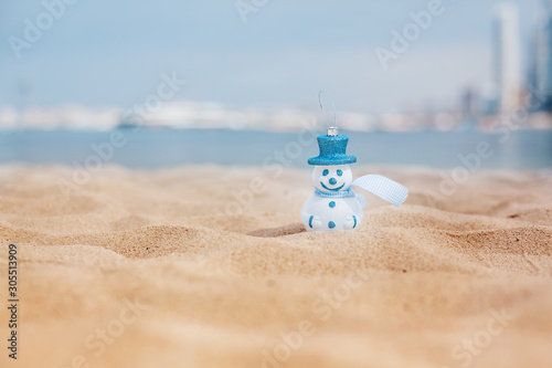 New Year's snowman in white in a blue hat on a background of a beautiful sea. Christmas and New Year holidays in the concept of warm countries.