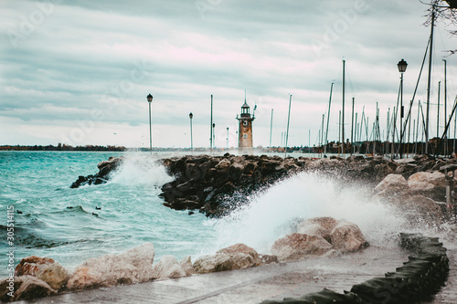 Picturesque landscape. Orange brick lighthouse during a storm on a lake with big waves, strong wind and heavy grey clouds on the coast of Lake Garda in the port of Desenzano del Garda, Lombardy, Italy