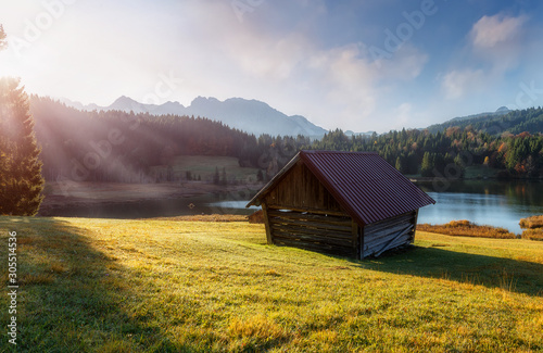 Magnificent sunny landscape in the Bavarian Alps.  a wooden hut on the shores of the Fairytale Lake Geroldsee under the rays of the morning sun. Wonderful Autumn landscape with colorful Sky.