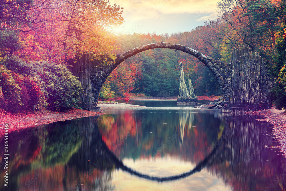 Plakat Niesamowity jesienny krajobraz. Niesamowity zachód słońca w Azalii i Rhododendron Park Kromlau. Rakotz Bridge, Rakotzbrucke Devil's Bridge w Kromlau, Saksonia, Niemcy. Kreatywny obraz artystyczny.