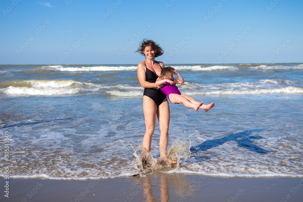Mother and daughter having fun on sea beach on summer vacation. Family on sea rest. Happy people in swimwear on beach Mother and daughter having fun on sea beach on summer vacation. Family on sea rest. Happy people in swimwear on beach
