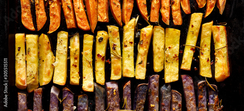 French fries, baked fries from different types and colors of potatoes sprinkled with herbs and spices on a black background, top view