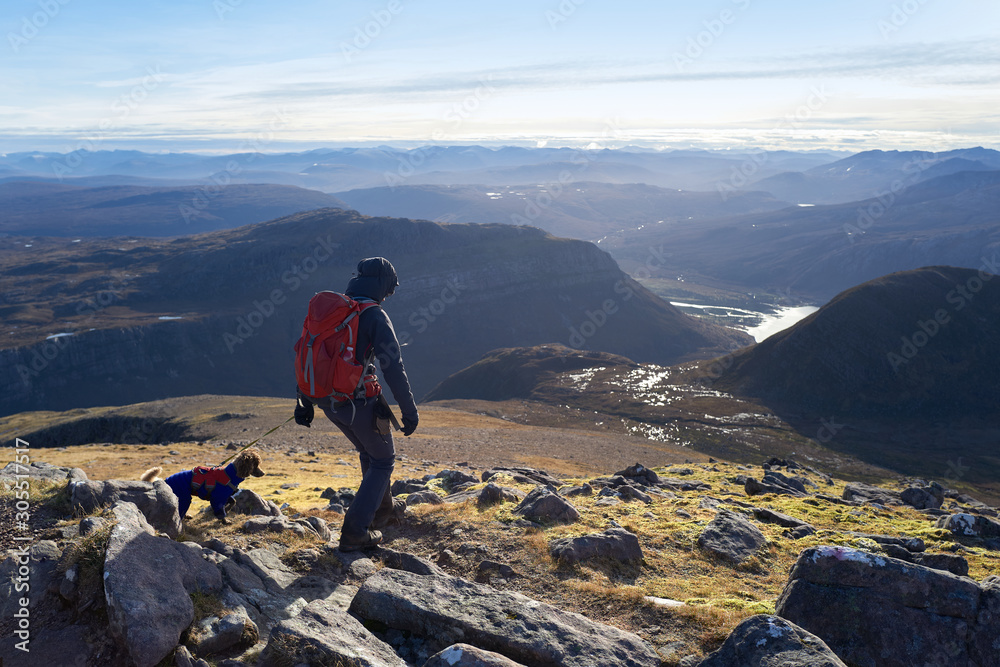 A hiker and their dog descending Sgurr an Tuill Bhain towards Coire na Sleaghaich above Kinlochewe in the distance in the Scottish Highlands.