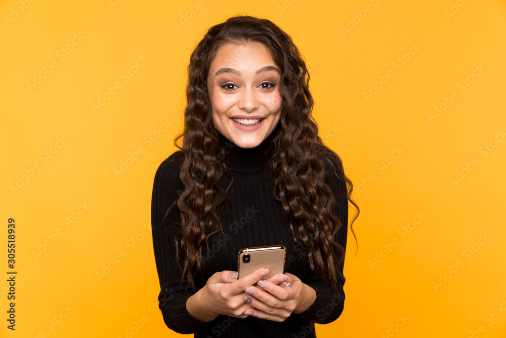 Young surprised and happy girl with mobile phone in the yellow studio isolated