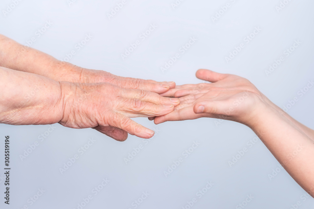 The hands of an old elderly grandmother and a child touch fingers in gestures on a white background. The concept of assistance, care and support for the elderly. The hands of an old elderly grandmother and a child touch fingers in gestures on a white background. The concept of assistance, care and support for the elderly.