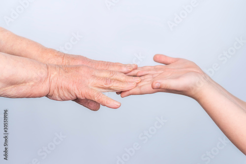 The hands of an old elderly grandmother and a child touch fingers in gestures on a white background. The concept of assistance, care and support for the elderly. © leksann