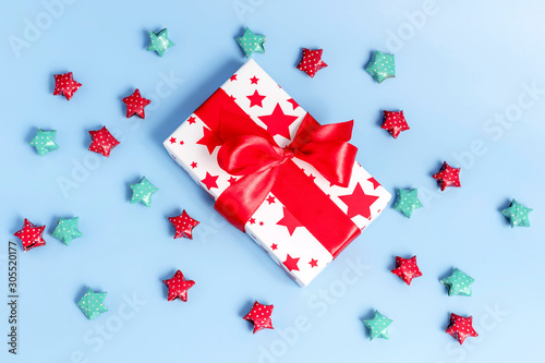 Gift box wrapped in kraft paper and multicolored stars on blue background. Top view, holiday concept.