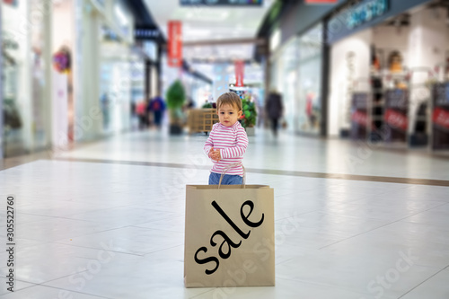 smart shopping concept. Close up of eco friendly paper bag with inscription sale. little cute baby girl standing in the mall and looking at a paper bag for shopping. soft focus, blur background