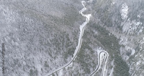 Aerial view of curvy road in the mountains cutting through snow covered forest. Winter landscape