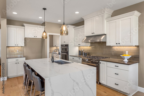 Beautiful kitchen in new luxury home with waterfall island, quartz counter tops, farmhouse sink, and hardwood floors.