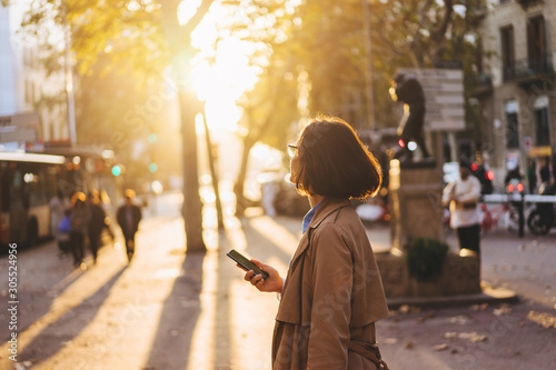 Girl enjoying sunset and chatting with friends via smartphone on the city streets photo