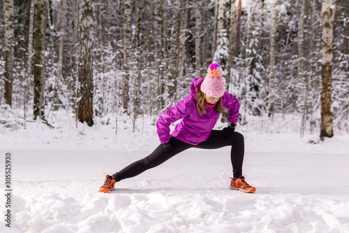 young woman warming up before jogging in a winter park