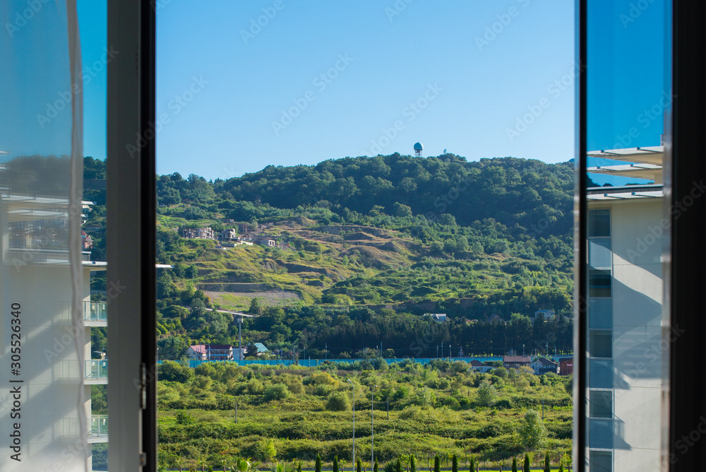 Fototapeta Widok na zielone wzgórza przez otwarte szklane drzwi balkonu.