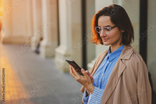 Portrait of attractive business woman checking messages on smartphone using 4g wireless for networking with sunset light glowing on left side