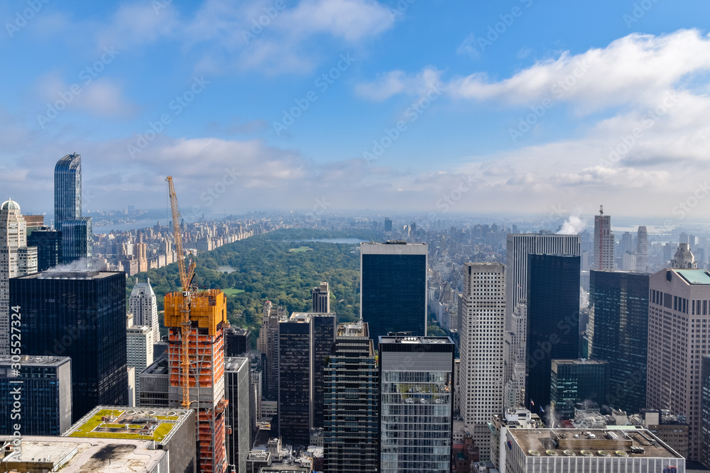 Fototapeta premium Aerial view of New York with skyscrapers, buildings in construction and central park in the background. Sunny day with some clouds. Concept of travel and construction. NYC, USA