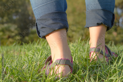Woman with flips and flops and jeans walking on grass.