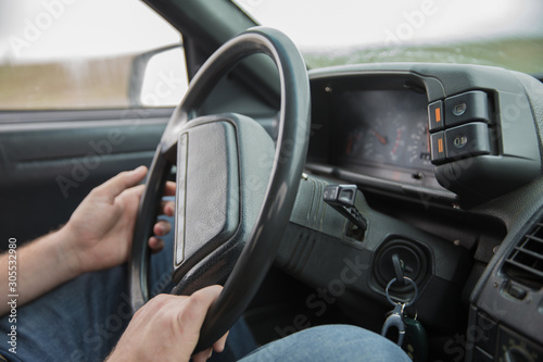 Car Interior. Male arms holding leathern rudder of car .the man grabs the steering wheel and drives the car. Black control panel in a old Russian car with a steering wheel . © Adil
