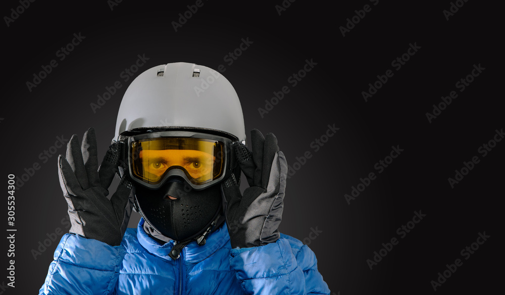 Skier wearing a ski helmet, google, gloves and a winter jacket on dark background. Concept of skiing, snowboarding. Winter sports.