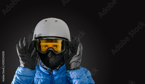 Skier wearing a ski helmet, google, gloves and a winter jacket on dark background. Concept of skiing, snowboarding. Winter sports.