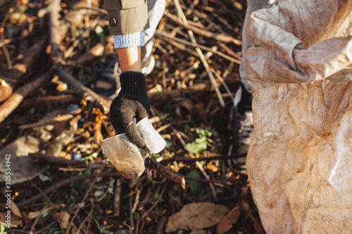 Eco activist picking up dirty plastic cups in park. Woman hand in glove picking up trash, collecting garbage in bag. Volunteer cleaning up nature from single use plastic photo