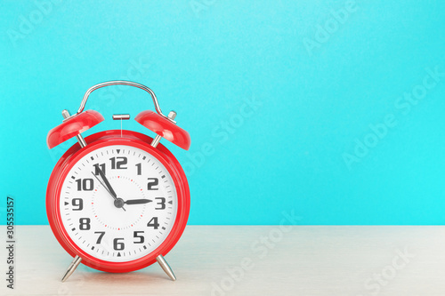 Red retro alarm clock with five minutes to three o'clock, on wooden table on a blue background. The concept of time, holiday, 5 minutes to the event, deadline. Layout with copy space for your text.