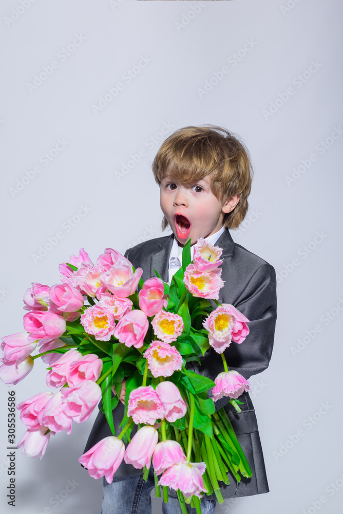 Surprised little boy with bouquet of tulips. Stylish little boy in elegant suit holds bouquet tulips. Gift to mum. Flower gift. Birthday, Women's Day, Mother's Day, Valentines day. Wedding concept. Surprised little boy with bouquet of tulips. Stylish little boy in elegant suit holds bouquet tulips. Gift to mum. Flower gift. Birthday, Women's Day, Mother's Day, Valentines day. Wedding concept.