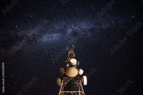From below wonderful view of media antenna and silhouettes of electricity high voltage power towers against night city on horizon and gorgeous Milky Way in clear sky photo