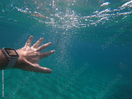 Close up of hand with smart watch underwater in the sea with rocks at the bottom. Thumbs up, while exercising abstract looking.