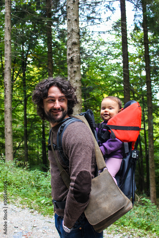 little girl is carried by her smiling dad in a backpack in the forest little girl is carried by her smiling dad in a backpack in the forest