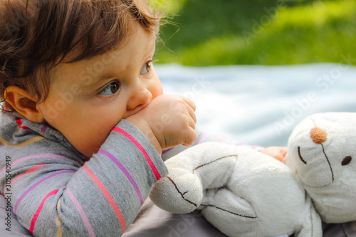 Tablou pe pânză adorable little baby girl eating her hand near her white teddy bear