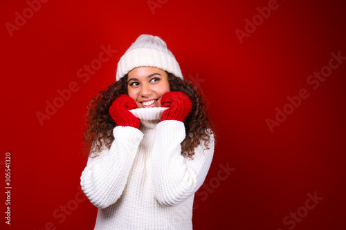Studio portrait of young woman with dark skin and long curly hair wearing knitted turtle neck sweater over the festive red wall with a lot of copy space for text. Close up  isolated background.