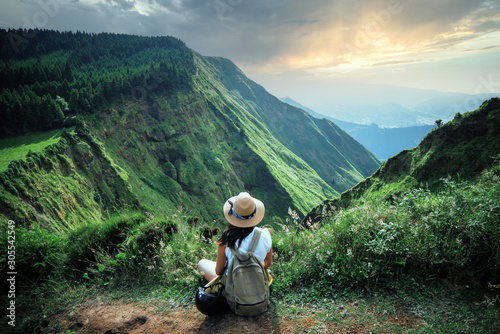 woman traveler holding hat and looking at amazing mountains and forest, wanderlust travel concept, space for text, atmospheric epic moment, azores ,portuhal, ponta delgada, sao miguel photo